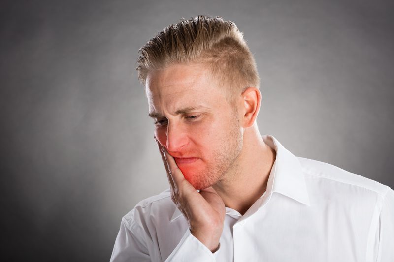 Man holding his cheek and frowning in pain.
